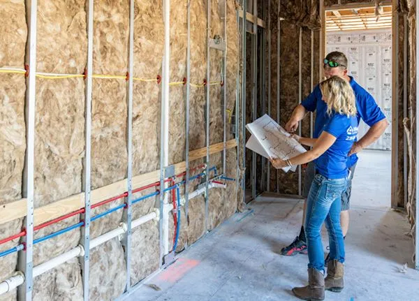 Man and woman standing in new home build reviewing blue prints in their hands