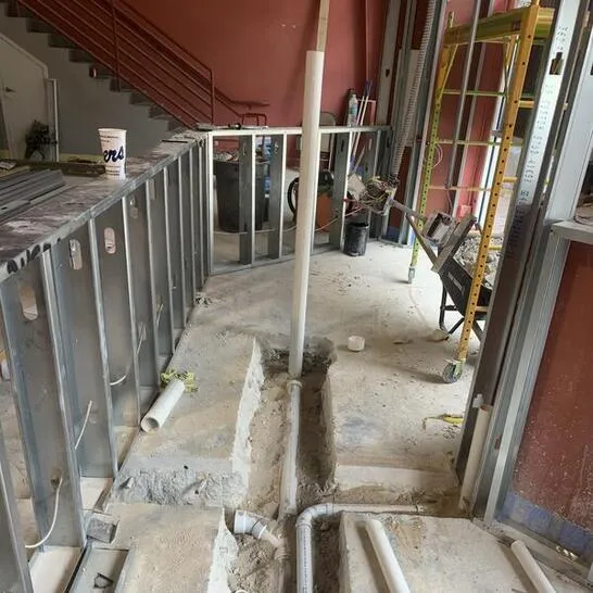 Home being remodeled with concrete floor chipped out for sewer line installation and waist high metal studs exposed