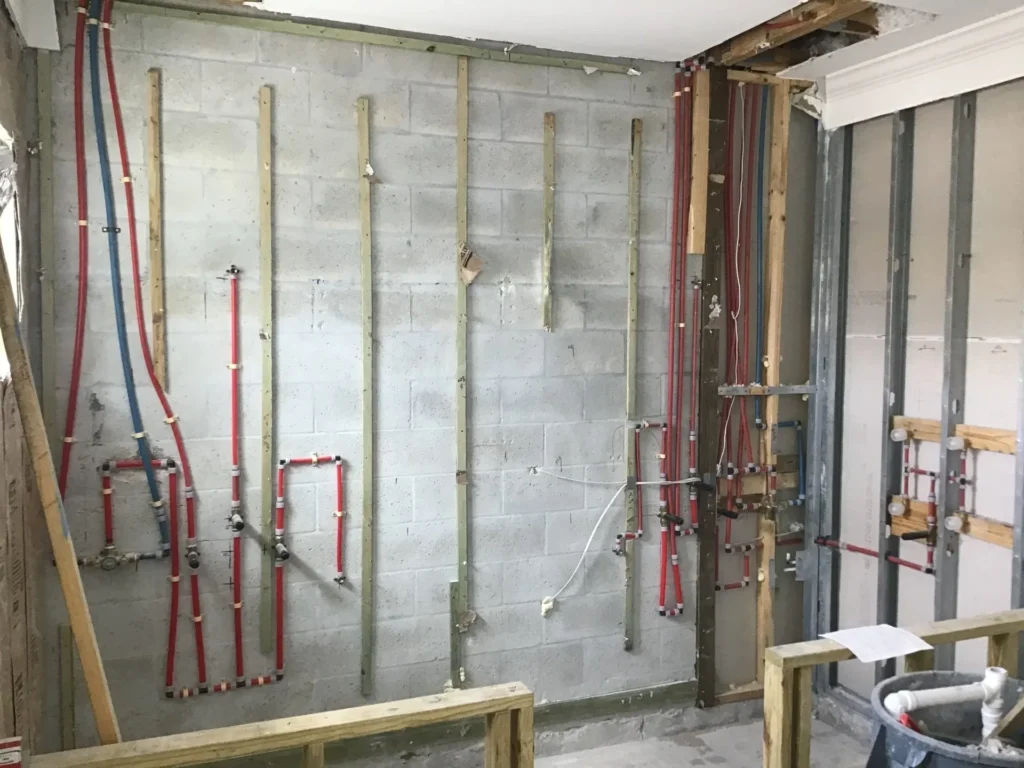 Bathroom with cinderblock walls exposed showing rough in plumbing phase with red pex water lines leading to shower valve fixtures