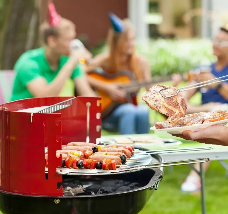 Close up picture of charcoal barbecue grille with sausages cooking and tongs holding a steak above the grille