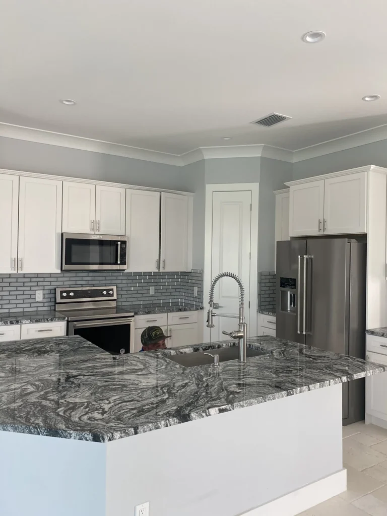 Plumber kneeling down in finished kitchen with granite countertops, white cabinets, stainless steel appliances and pull down kitchen faucet