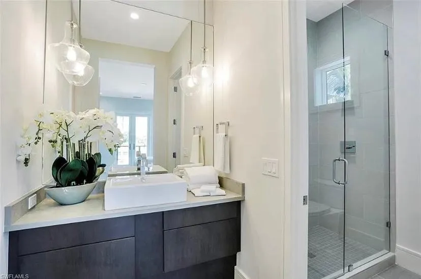 Finished bathroom with single vessel sink on top of dark brown cabinets, vase with white flowers next to vessel sink, with walk in shower to the right of vanity