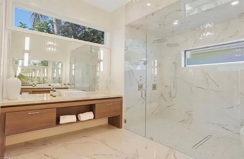 Finished bathroom with wood vanity, white marble floor tile, white marble shower walls and frameless glass shower doors custom shower drain