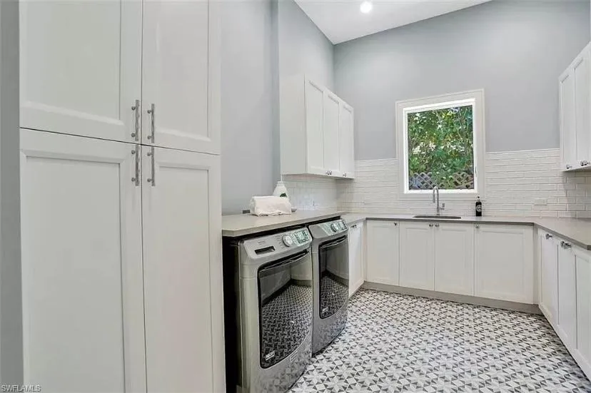 Finished laundry room with picture frame window, white cabinets, laundry sink, light brown quartz countertops, tile floor and new wash and dryer machines