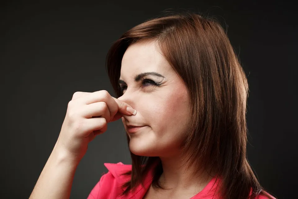 Woman in red shirt holding her nose due to a foul smell