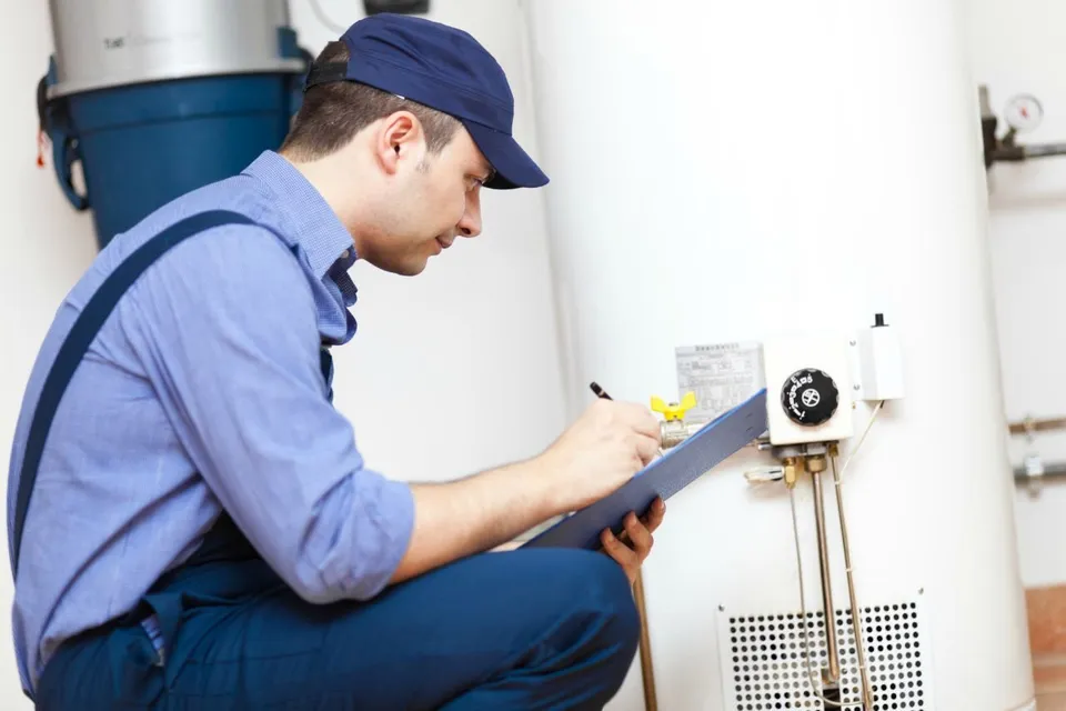 Plumber kneeling down taking notes on clipboard next to water heater